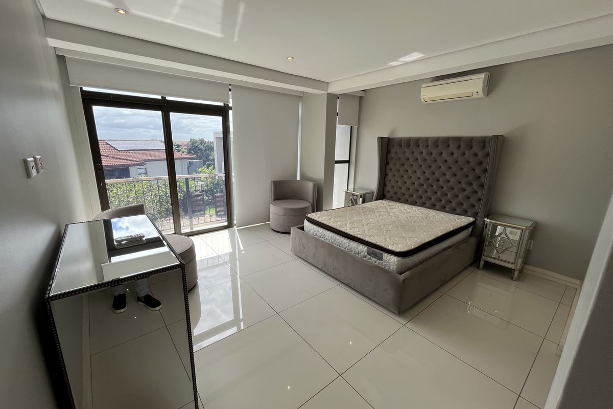 Spacious bedroom featuring large format floor tiles, recessed ceiling lighting, a wall-mounted air conditioning unit, and sliding glass doors leading to a private balcony.