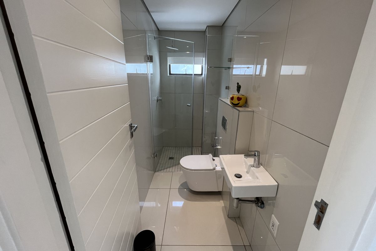 Modern compact bathroom featuring floor-to-ceiling tiling, a wall-mounted toilet, a sleek vanity basin, and a glass-enclosed walk-in shower.