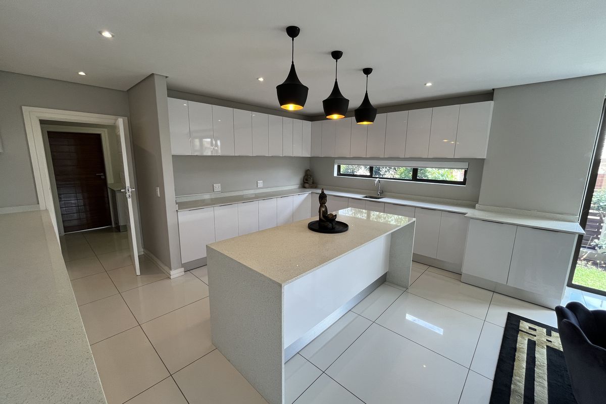 Modern kitchen featuring high-gloss white cabinetry, stone countertops, a central island, and sleek pendant lighting, finished with polished floor tiles.