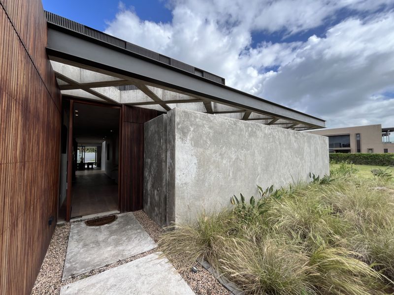 Modern architectural entrance featuring a striking concrete facade, timber cladding, and a steel-framed roof structure leading into the home.