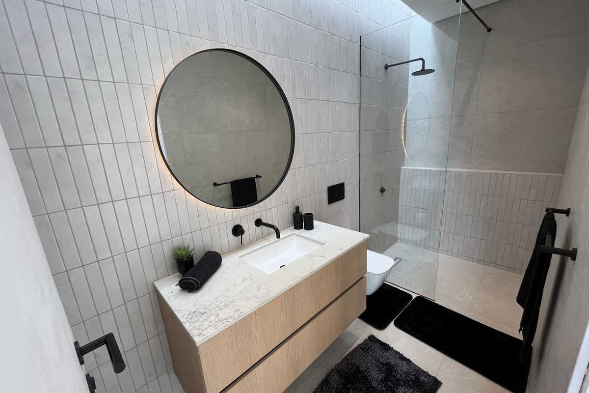 Modern bathroom featuring a floating timber vanity with stone countertop, frameless glass walk-in shower, and contemporary matte black fixtures.