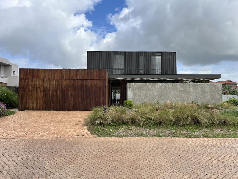 Modern architectural residence featuring a striking combination of rusted metal cladding, concrete walls, and dark vertical timber slats with a paved driveway.