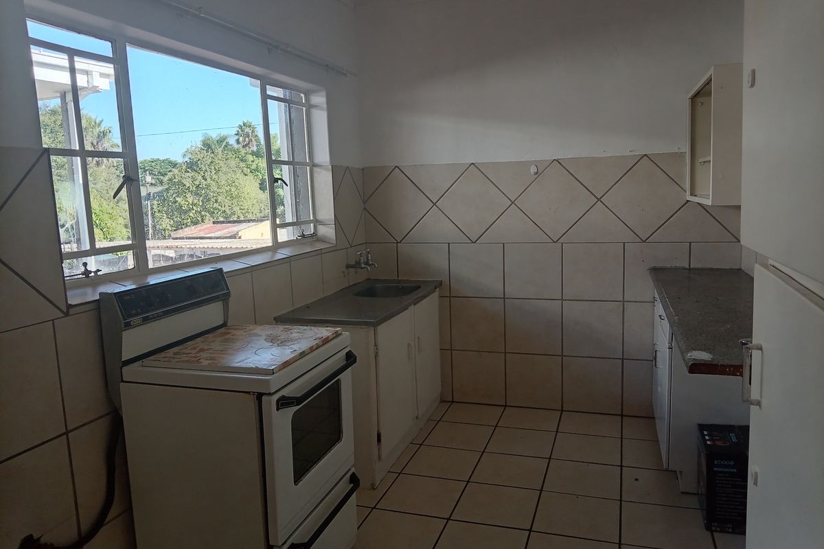A dated kitchen featuring original cabinetry, tiled walls, and floor, with a freestanding stove and a window providing natural light.