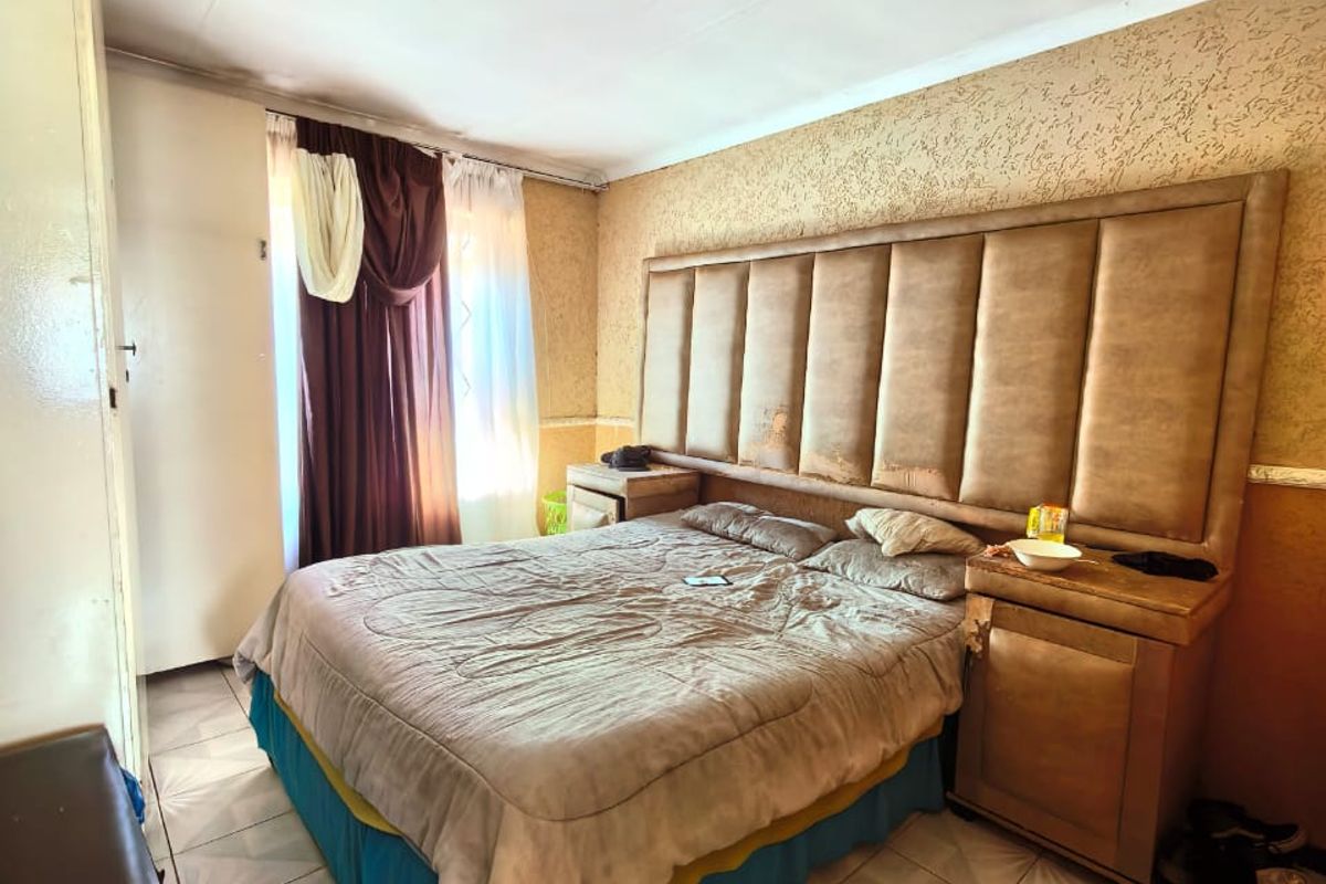 A bedroom featuring a large built-in upholstered headboard, tiled flooring, and a ceiling-mounted light fixture.