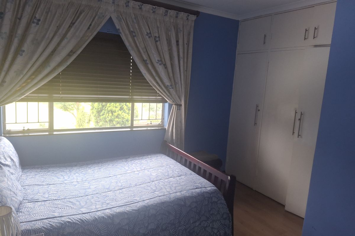 A bedroom featuring built-in cupboards, laminate flooring, and a window with blinds, providing a functional living space.