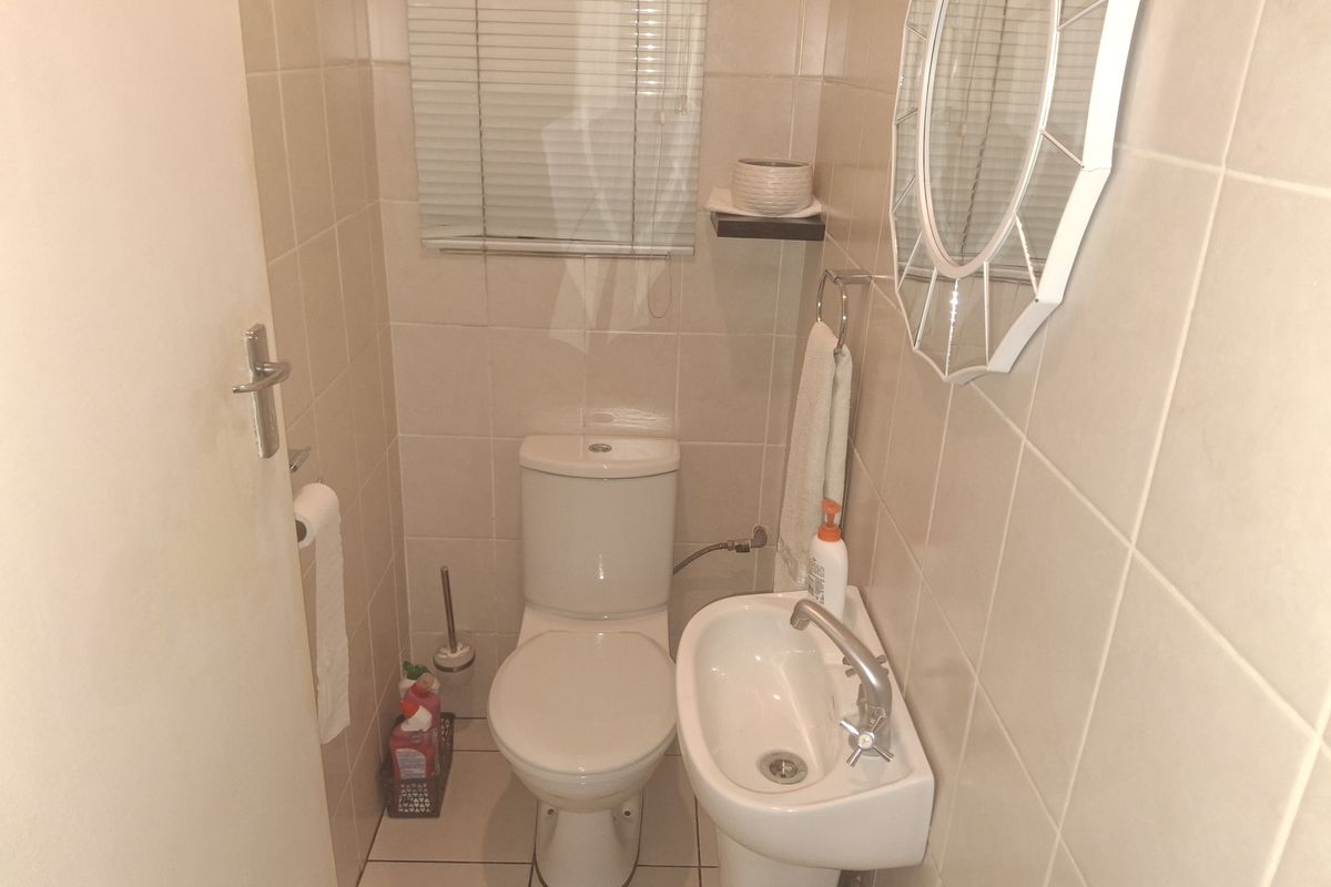 A compact guest bathroom featuring floor-to-ceiling wall tiles, a pedestal basin, and a standard toilet.