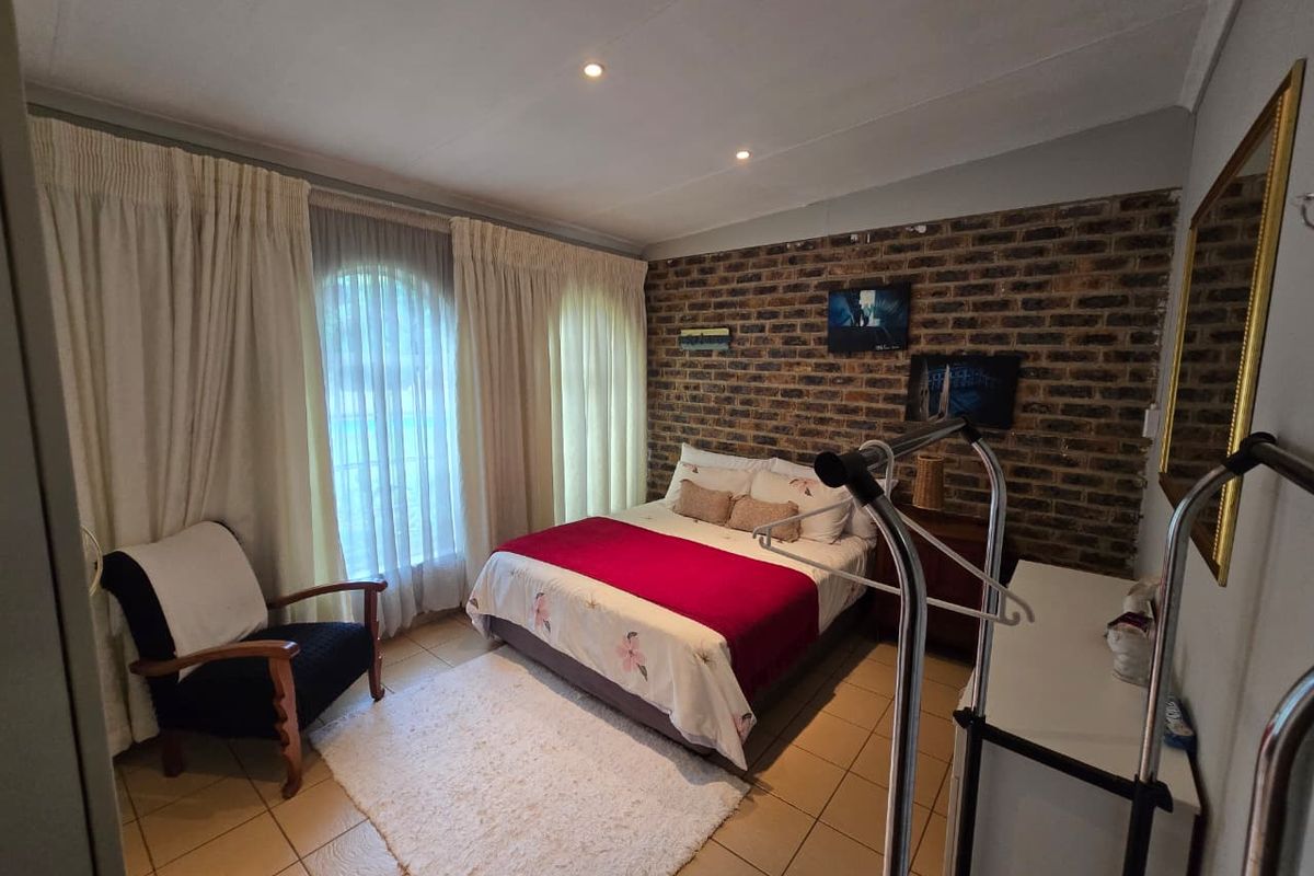 A bedroom featuring a rustic exposed brick feature wall, tiled flooring, and large windows with floor-to-ceiling curtains.