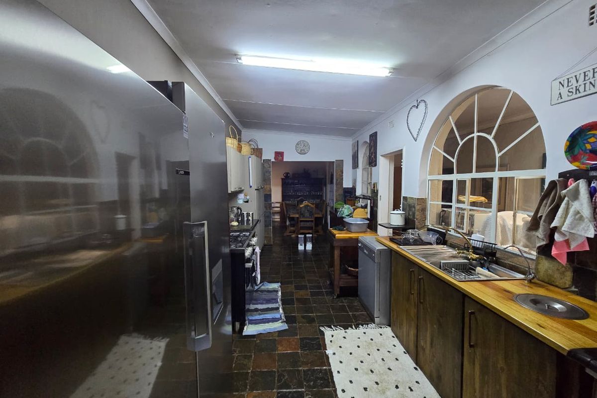 A functional kitchen featuring wooden cabinetry, a double sink, and a distinctive arched window, leading through to an open-plan dining area.
