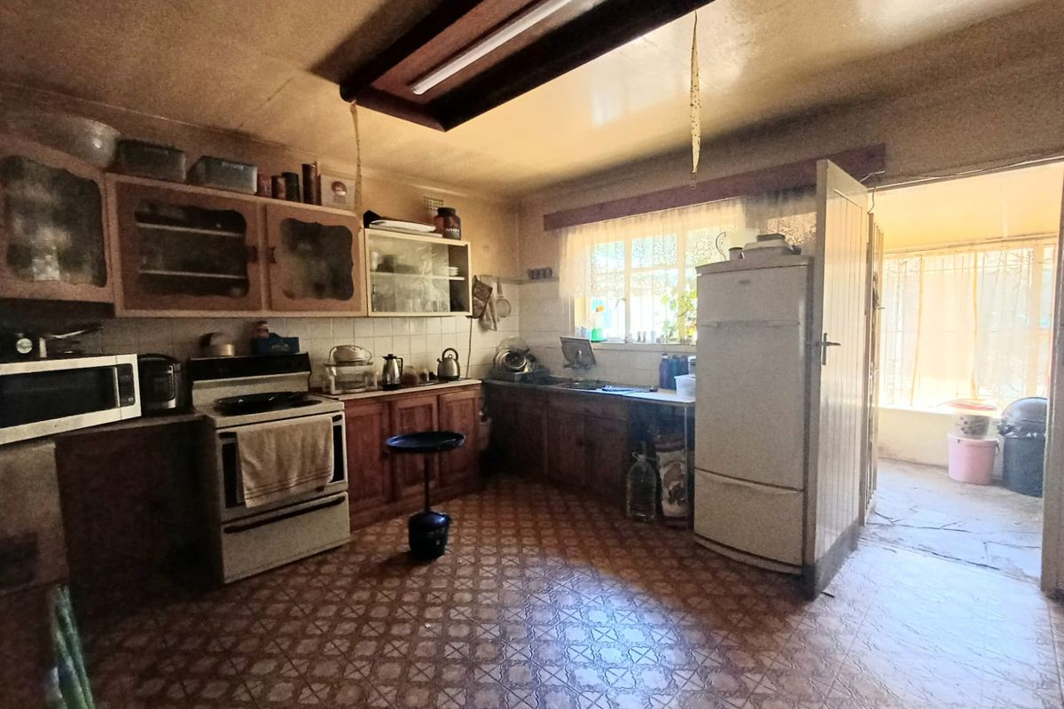 A dated kitchen featuring original wooden cabinetry, tiled flooring, and a functional layout with direct access to an adjacent outdoor area.
