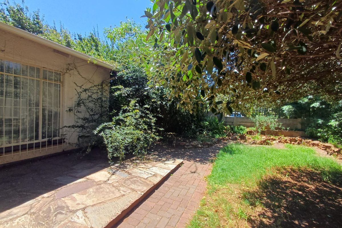 A rear garden area featuring a paved patio, established trees, and a lawn, providing a private outdoor space adjacent to the house.