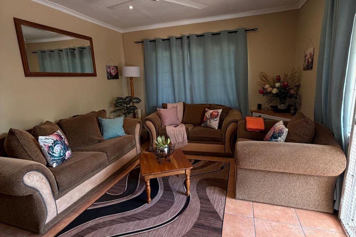 A comfortable living room featuring tiled flooring, a ceiling fan, and large windows with curtain tracks.