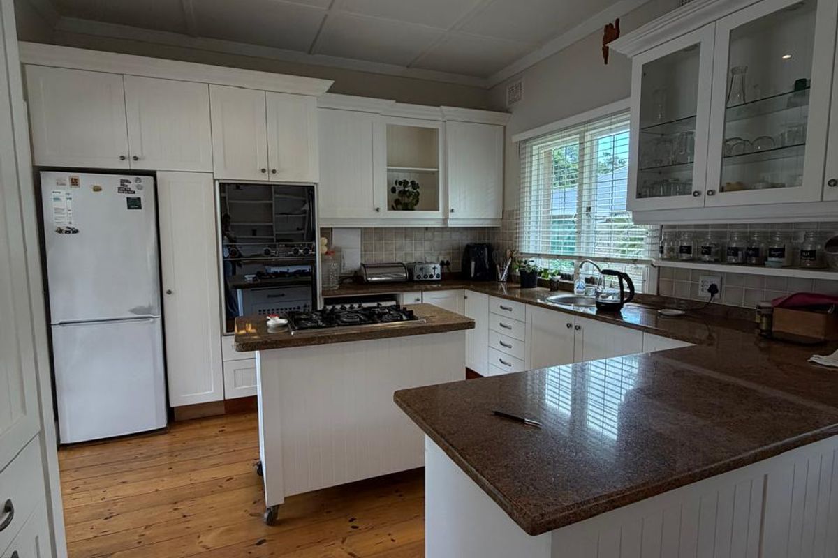 A well-maintained kitchen featuring white cabinetry, granite countertops, a central island, and warm timber flooring under a panelled ceiling.