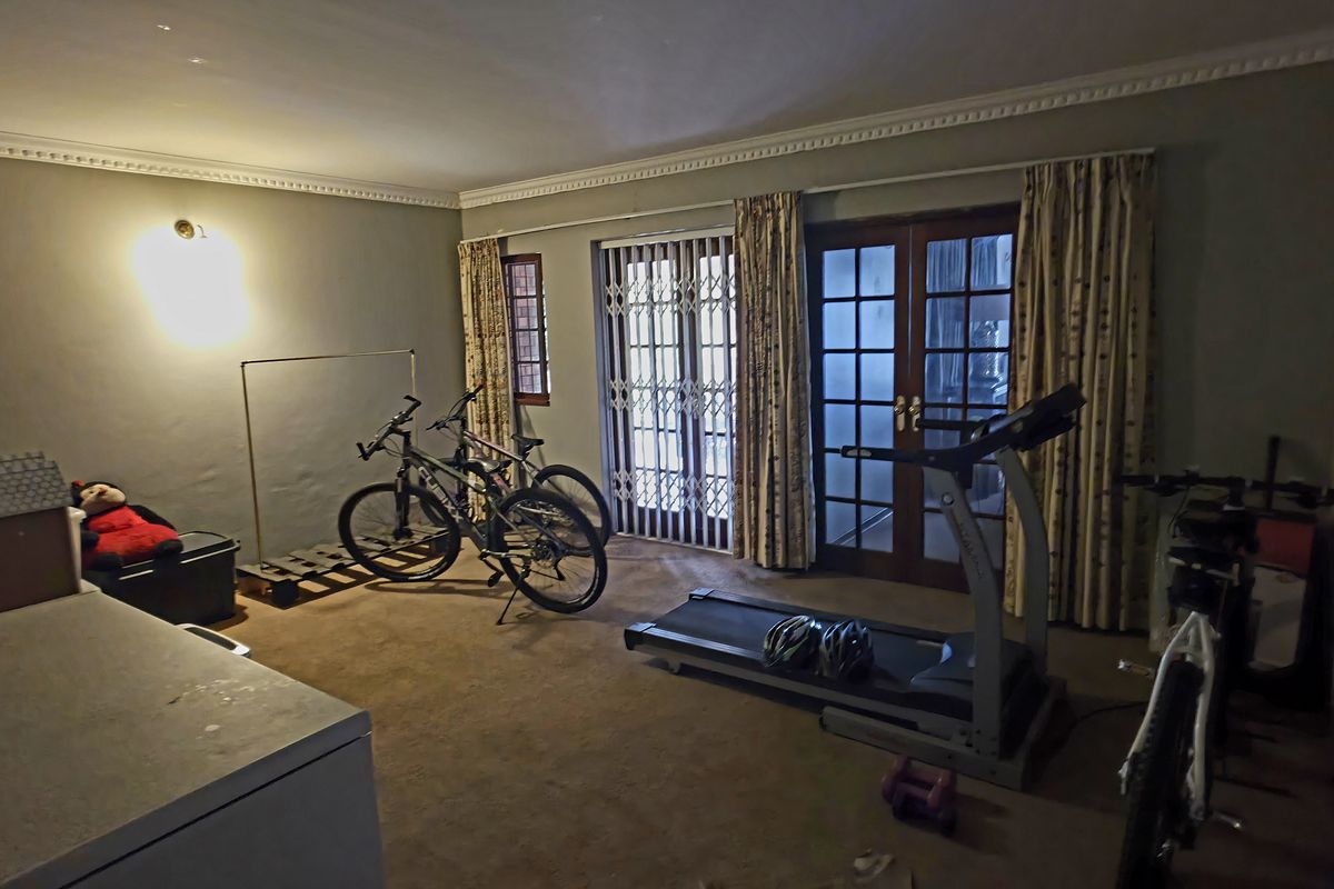 A living room featuring carpet flooring, decorative cornice, and double french doors leading to the exterior with security gates.
