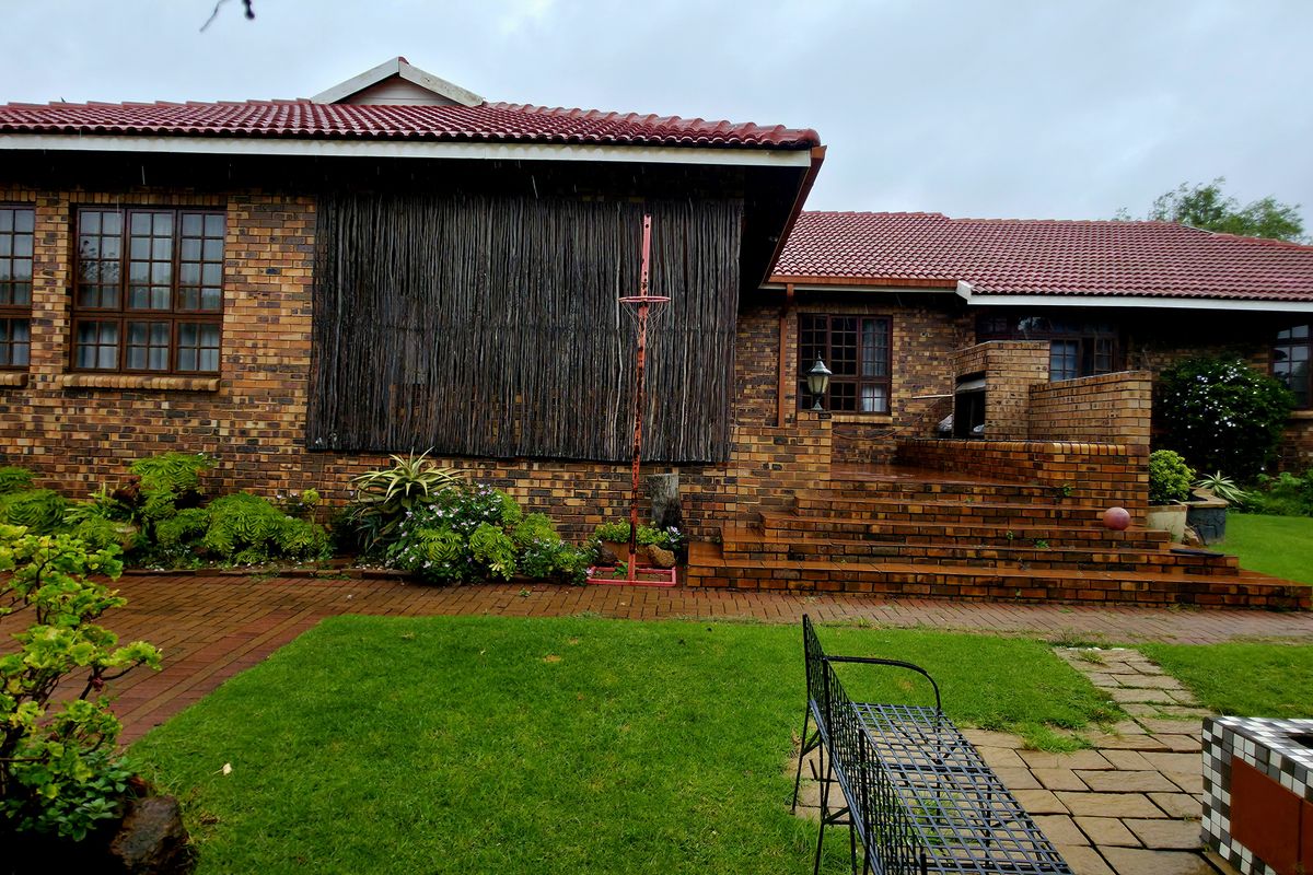 Rear view of a face brick house featuring a tiled roof, paved patio area, and a built-in fire pit set within a landscaped garden.
