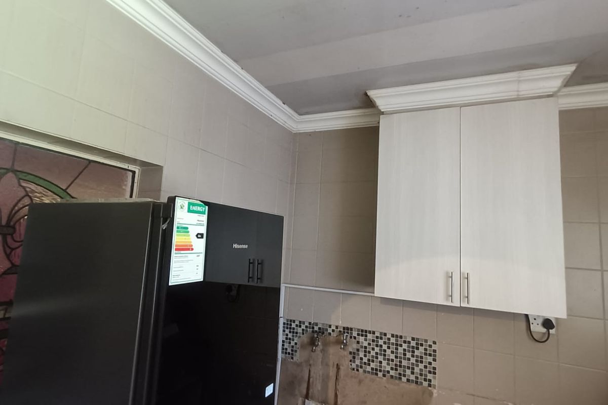 A kitchen area featuring wall-mounted cabinetry, tiled walls, and exposed plumbing connections, requiring finishing work to complete the backsplash and wall surfaces.
