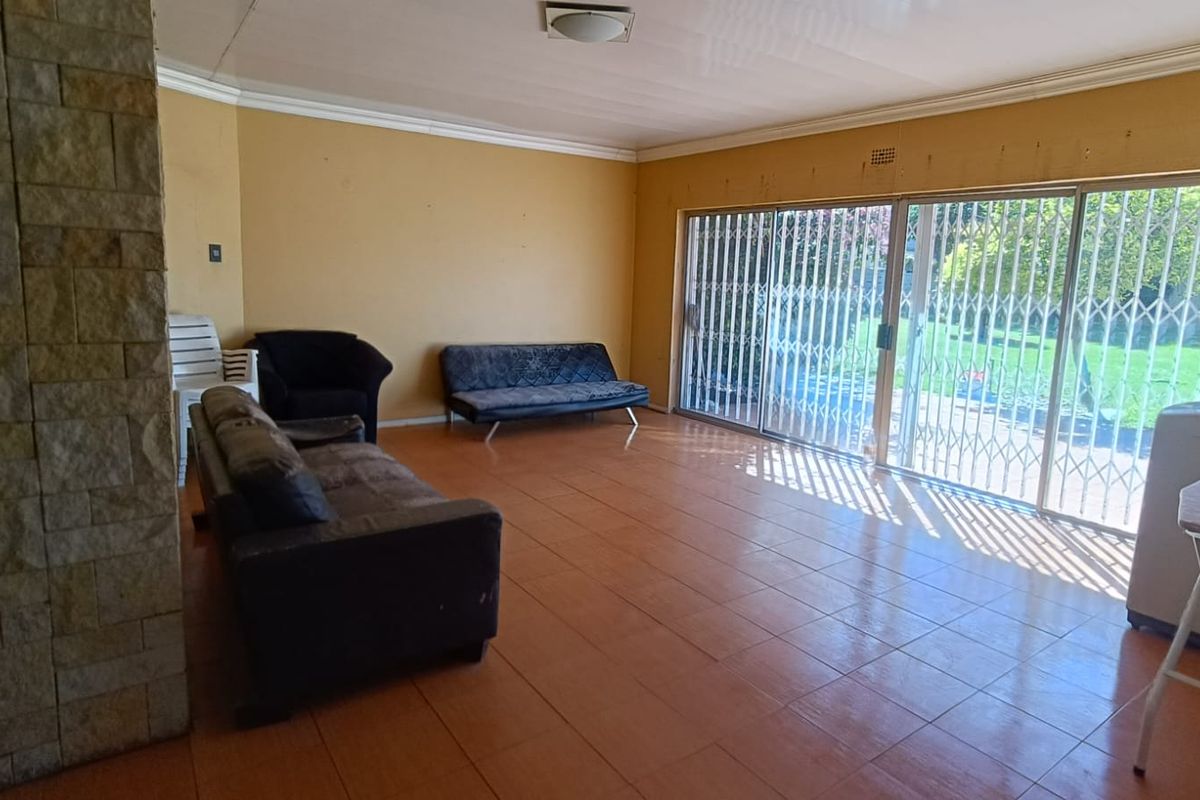 Spacious living area featuring tiled flooring, a stone-clad feature wall, and large sliding glass doors with security gates leading to the garden.