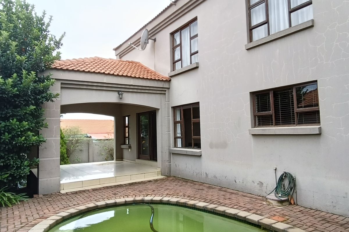 Rear exterior view featuring a covered patio, paved pool area, and two-story building facade with visible wall cracking and maintenance requirements.