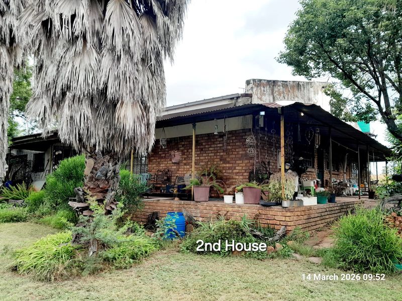 Exterior view of a rustic farm dwelling featuring a covered brick patio, exposed brick walls, and a corrugated metal roof structure.