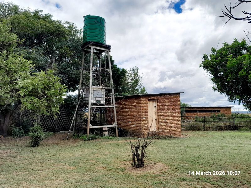 Outdoor utility area featuring a raised water storage tank on a metal stand adjacent to a small brick structure on the farm property.