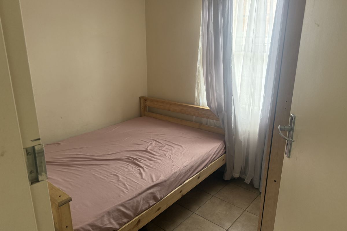 A compact bedroom featuring tiled flooring and a window with curtain fixtures, providing a functional and simple living space.