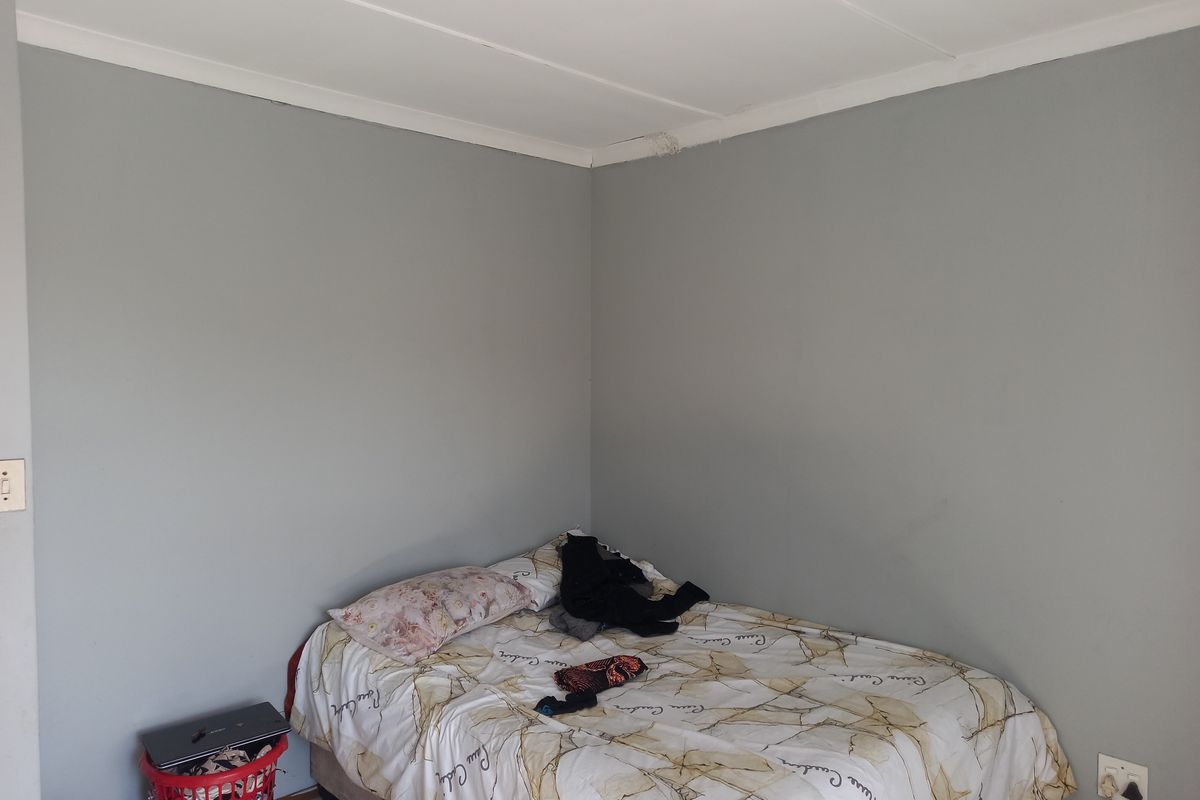 A simple bedroom featuring neutral grey walls, tiled flooring, and standard ceiling cornicing.