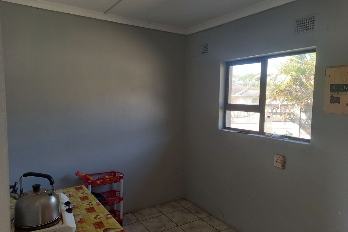 A basic kitchen area featuring tiled flooring, a window with natural light, and an electrical outlet, providing a functional space for culinary activities.