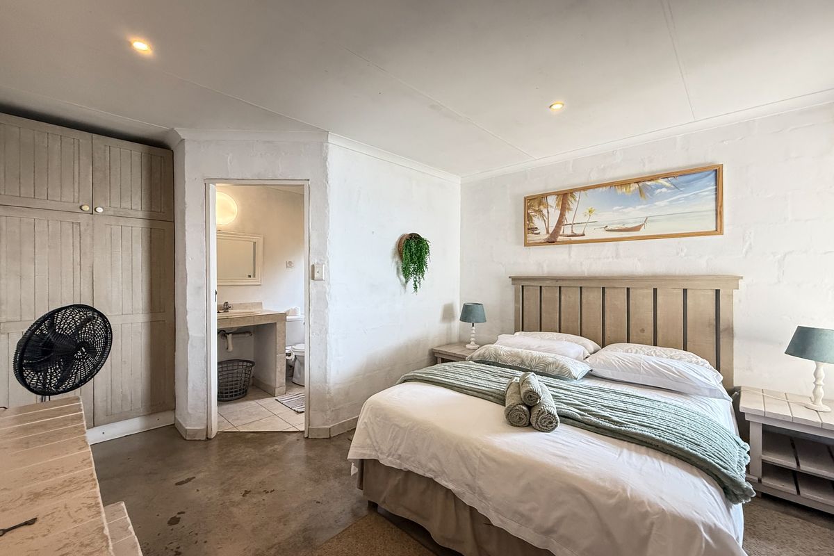 A bedroom featuring a built-in wardrobe, exposed concrete flooring, and an en-suite bathroom with a vanity and toilet.
