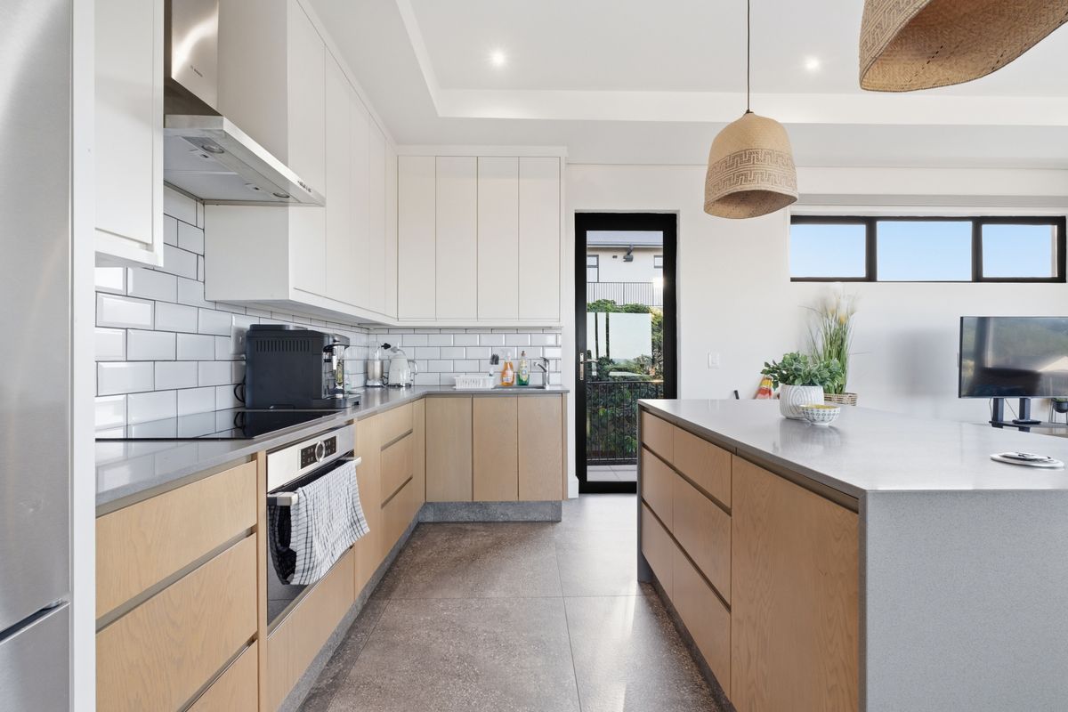 Modern kitchen featuring light wood cabinetry, stone countertops, subway tile backsplash, built-in oven, extractor fan, and a central island with breakfast bar seating.