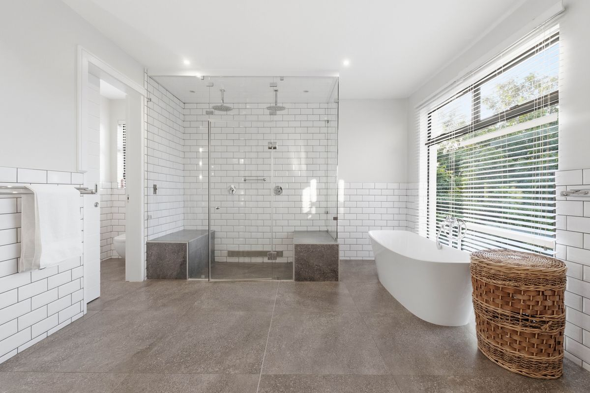 Modern bathroom featuring a large walk-in glass shower with dual rainfall showerheads, built-in stone benches, and a freestanding soaking tub.