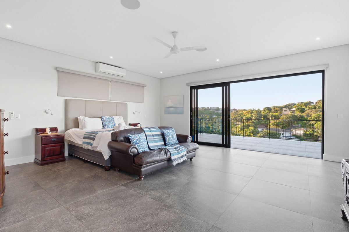Spacious bedroom featuring large format floor tiles, ceiling fan, split-system air conditioning, and sliding glass doors opening to a private balcony with scenic views.