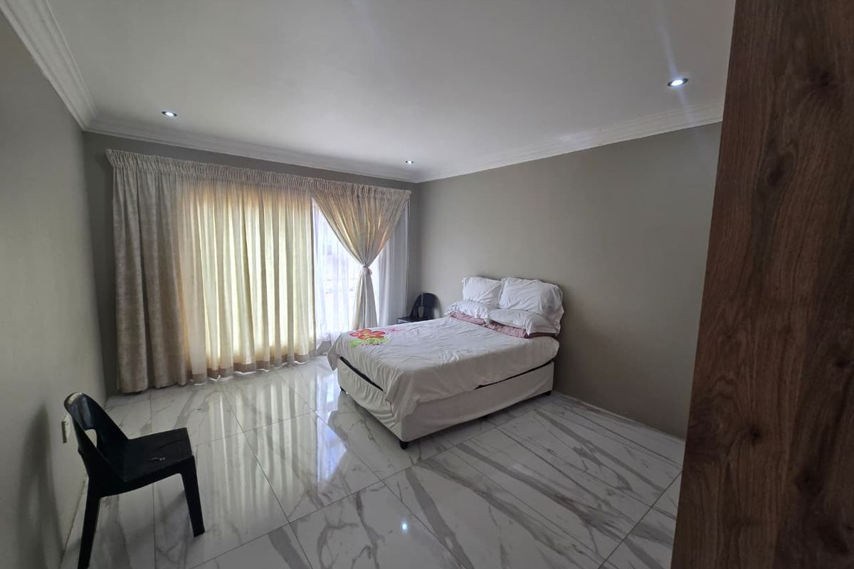 A spacious bedroom featuring modern marble-look floor tiles, recessed ceiling lighting, and large sliding glass doors with floor-to-ceiling curtains.