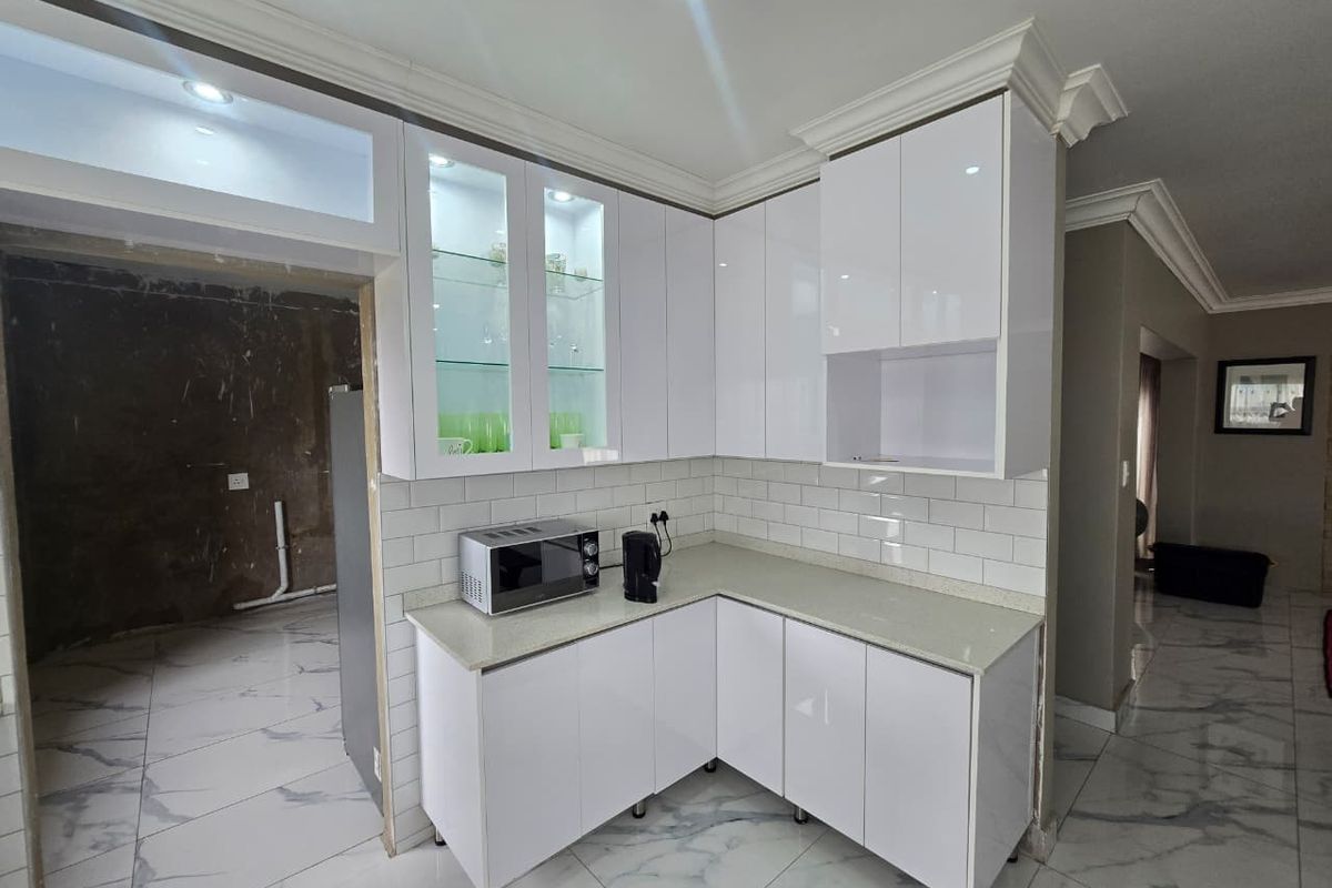 Modern kitchen featuring white high-gloss cabinetry, stone countertops, and subway tile backsplash, with an adjacent unfinished utility area.