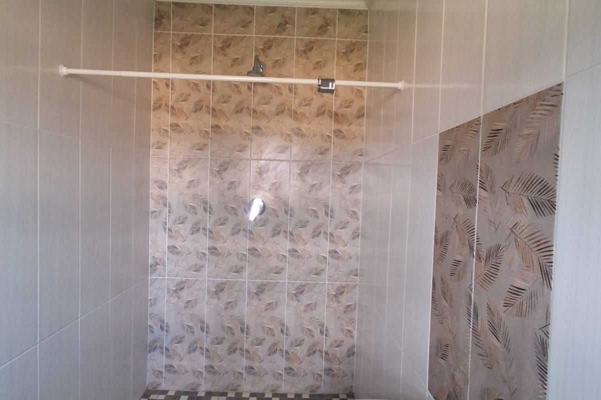 A compact bathroom featuring a walk-in shower with decorative tiled accents and a wall-mounted basin.