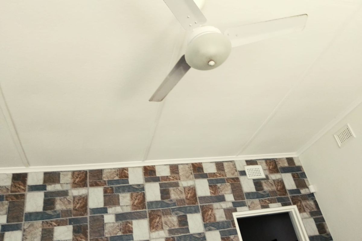 A room interior featuring a ceiling fan and a decorative tiled feature wall with a standard doorway and ventilation vent.