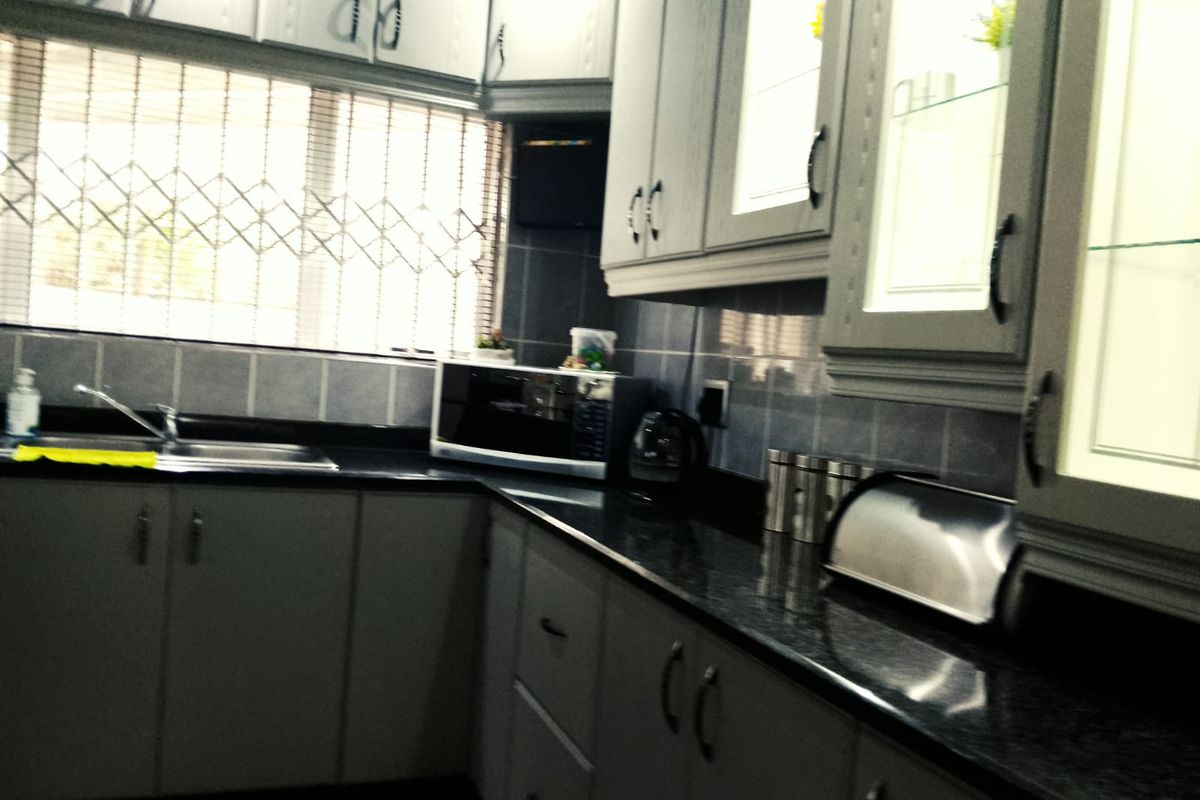 A functional kitchen featuring dark granite countertops, grey cabinetry, tiled splashbacks, and a stainless steel sink with a window security gate.