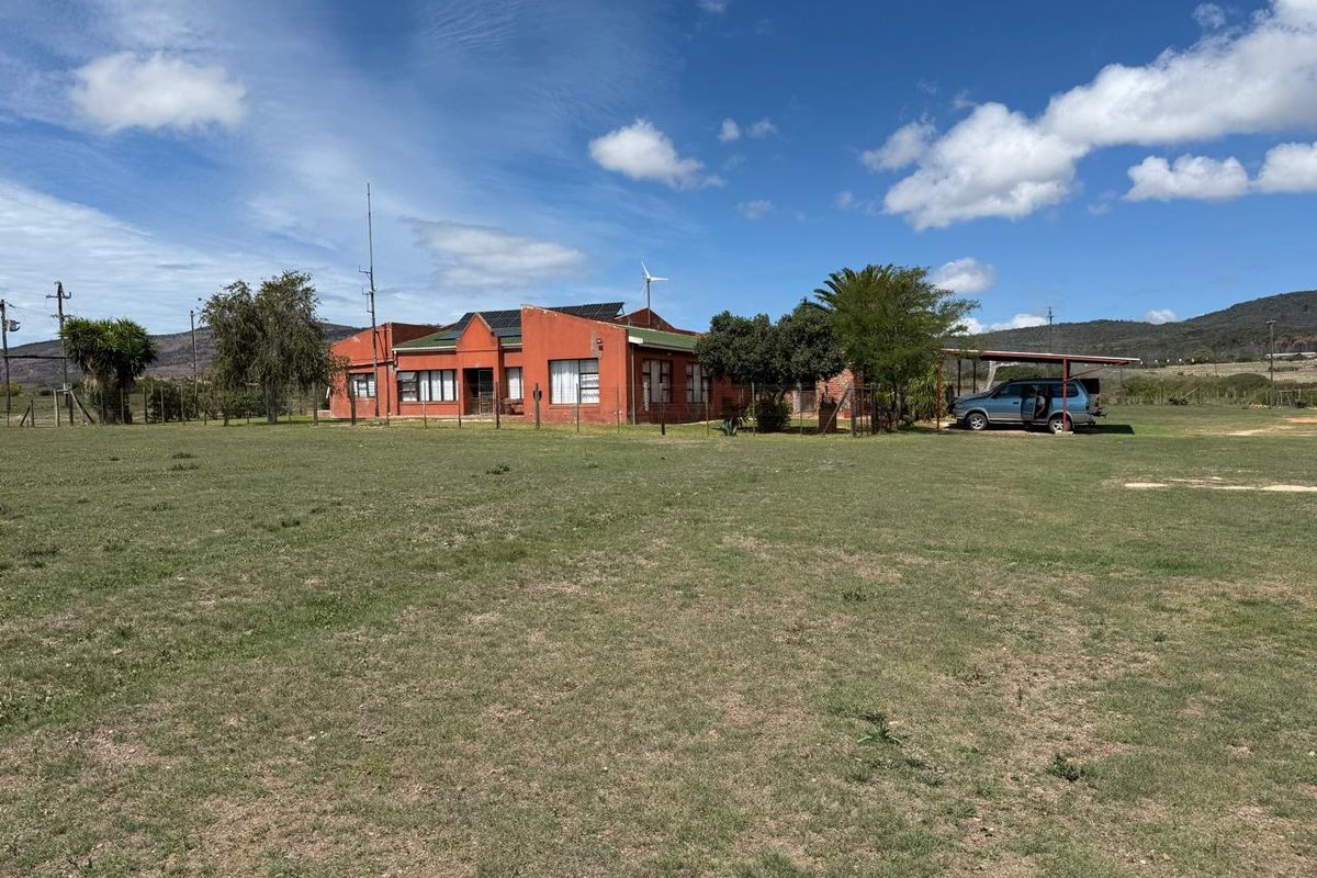 A wide-angle view of the rear farm property featuring a red brick dwelling, solar panels, a small wind turbine, and an attached carport.