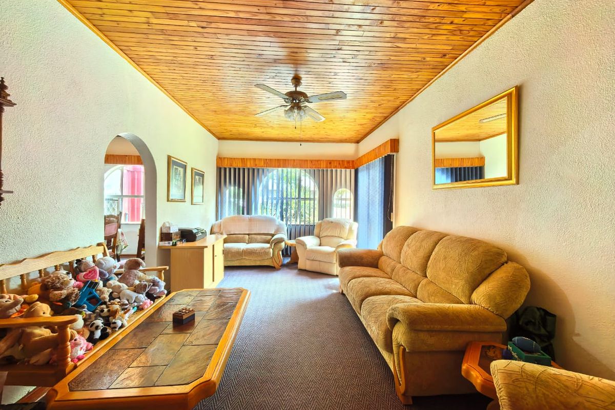 A traditional living room featuring a timber-clad ceiling, ceiling fan, and arched doorway leading to an adjacent space.