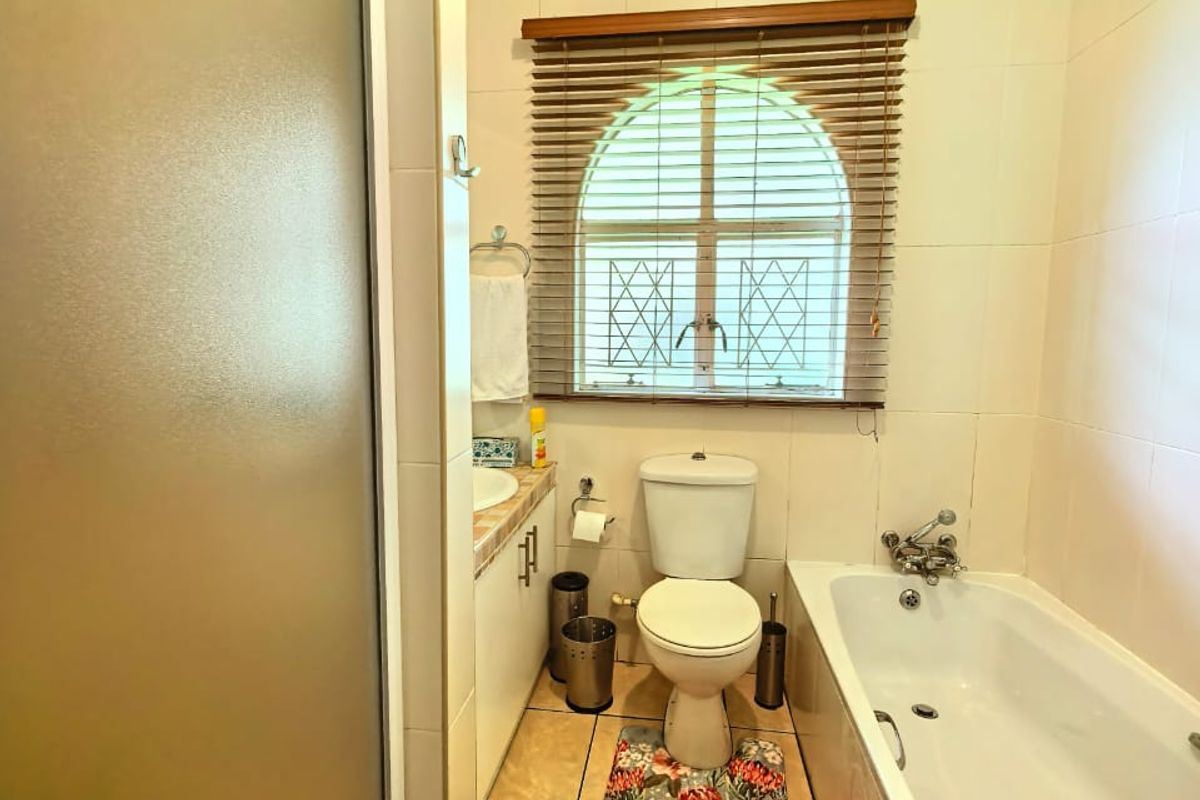 A functional bathroom featuring a bathtub, separate shower enclosure, toilet, and vanity basin with a window providing natural light.