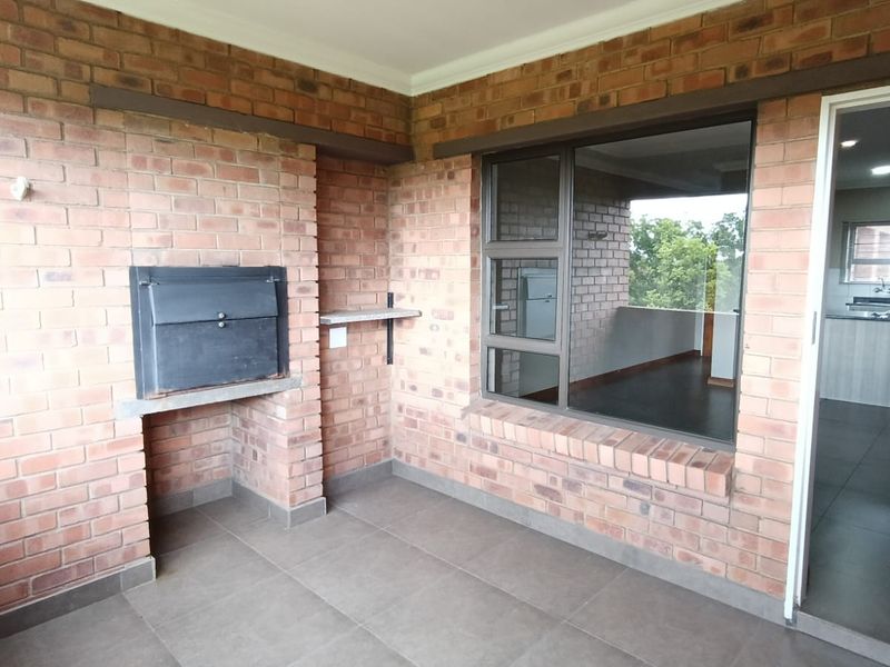 Covered balcony featuring a built-in braai, exposed brick walls, and tiled flooring, offering a functional outdoor entertainment space.