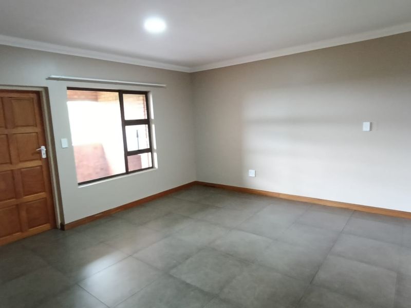 A spacious, empty living area featuring neutral wall tones, large windows, and modern tiled flooring, providing a clean canvas for interior design.
