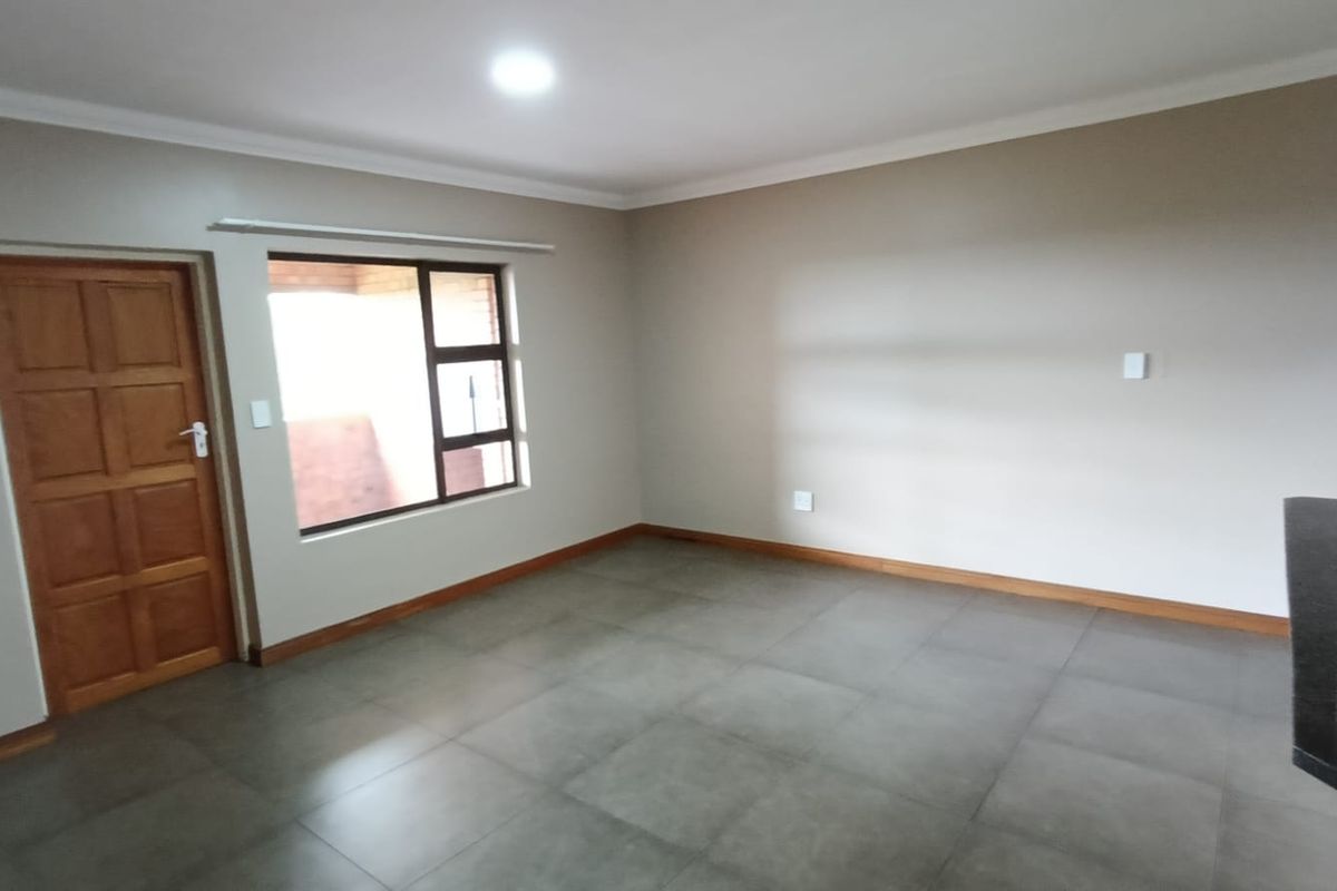 A spacious, empty living area featuring neutral wall tones, large windows, and modern tiled flooring, providing a clean canvas for interior design.