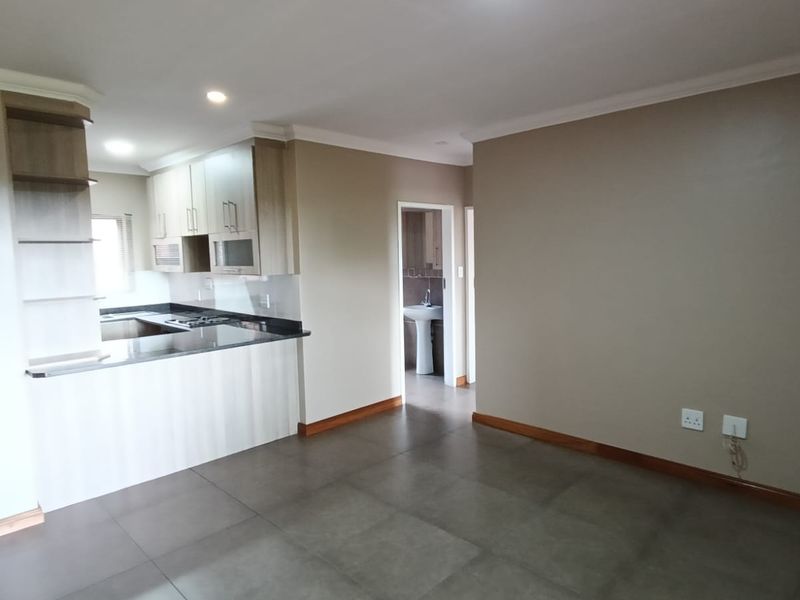 Open-plan living area featuring a modern kitchen with granite countertops, hob, and extractor fan, leading to a tiled space with neutral wall finishes.