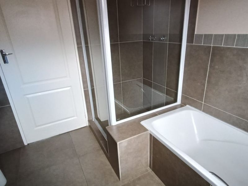 A clean, modern bathroom featuring a pedestal basin, a separate shower enclosure, and a built-in bathtub with neutral-toned wall and floor tiling.