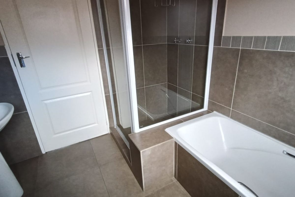 A clean, modern bathroom featuring a pedestal basin, a separate shower enclosure, and a built-in bathtub with neutral-toned wall and floor tiling.