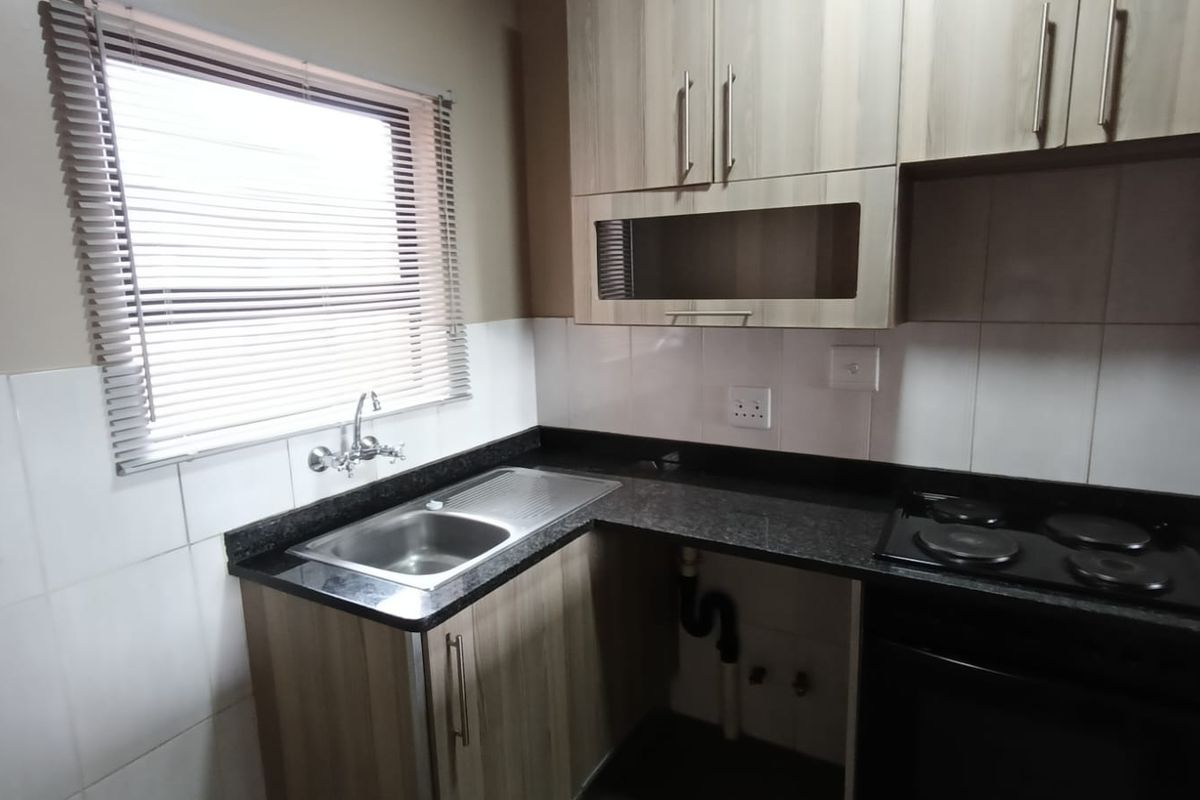 A functional kitchen featuring laminate cabinetry, granite countertops, a built-in oven, electric hob, and a stainless steel sink with tiled splashback.