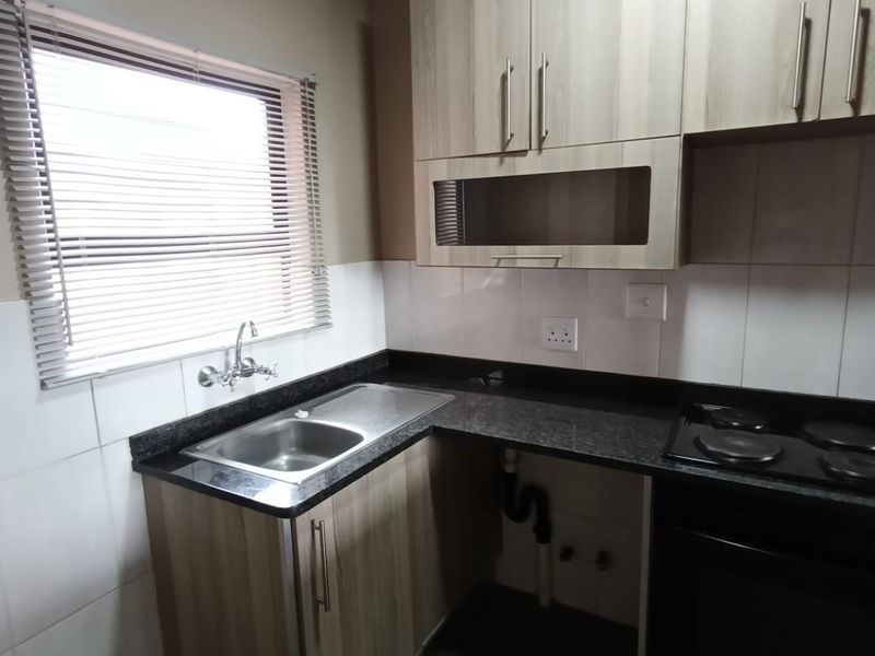 A functional kitchen featuring laminate cabinetry, granite countertops, a built-in oven, electric hob, and a stainless steel sink with tiled splashback.