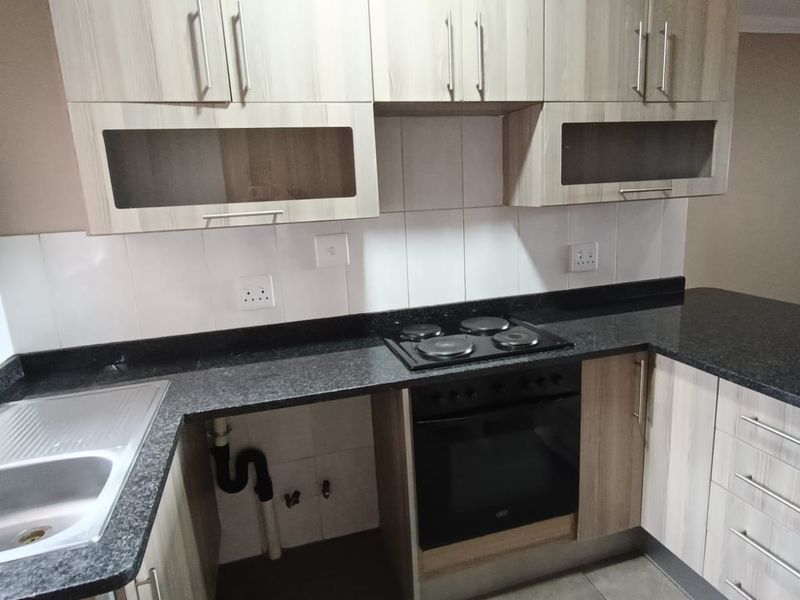 A functional kitchen featuring laminate cabinetry, granite countertops, a built-in oven, and an electric hob, with an open space for an under-counter appliance.