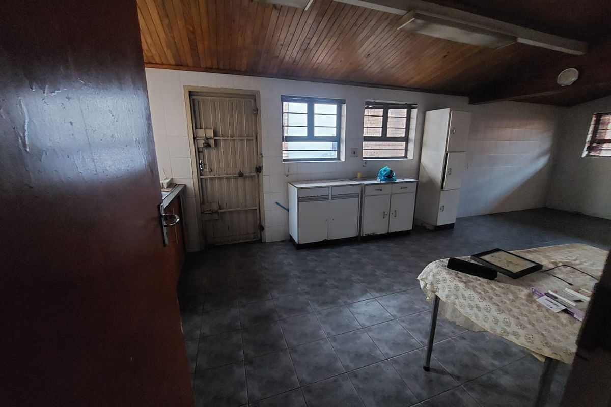 A dated kitchen area featuring tiled flooring, wooden ceiling paneling, and basic built-in cabinetry with a security door leading to the exterior.