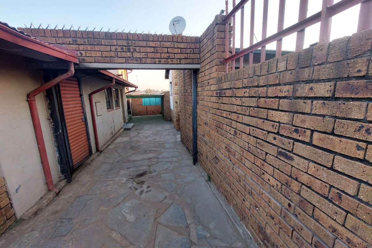 A side passage featuring stone paving, enclosed by brick boundary walls with security spikes and a satellite dish mounted above the walkway.