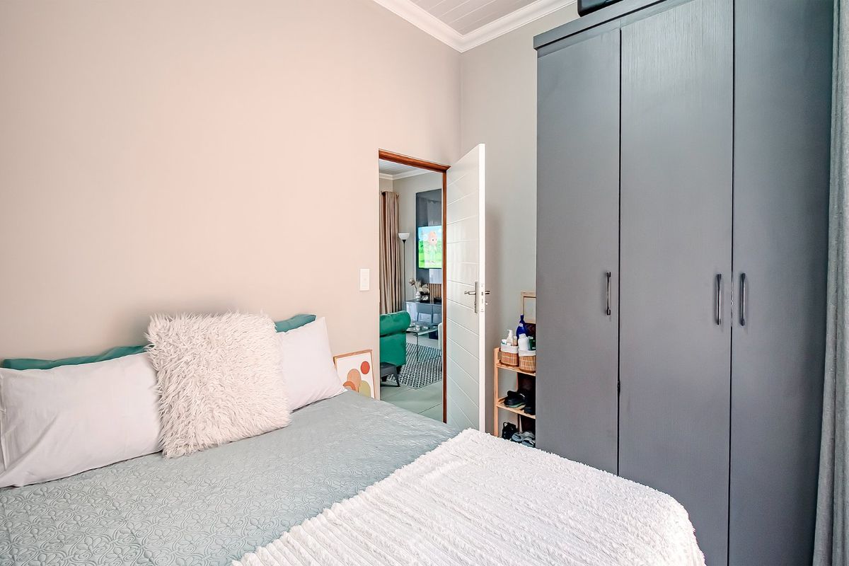 A well-maintained bedroom featuring built-in grey cabinetry and neutral wall finishes, with a view into the adjacent living area.